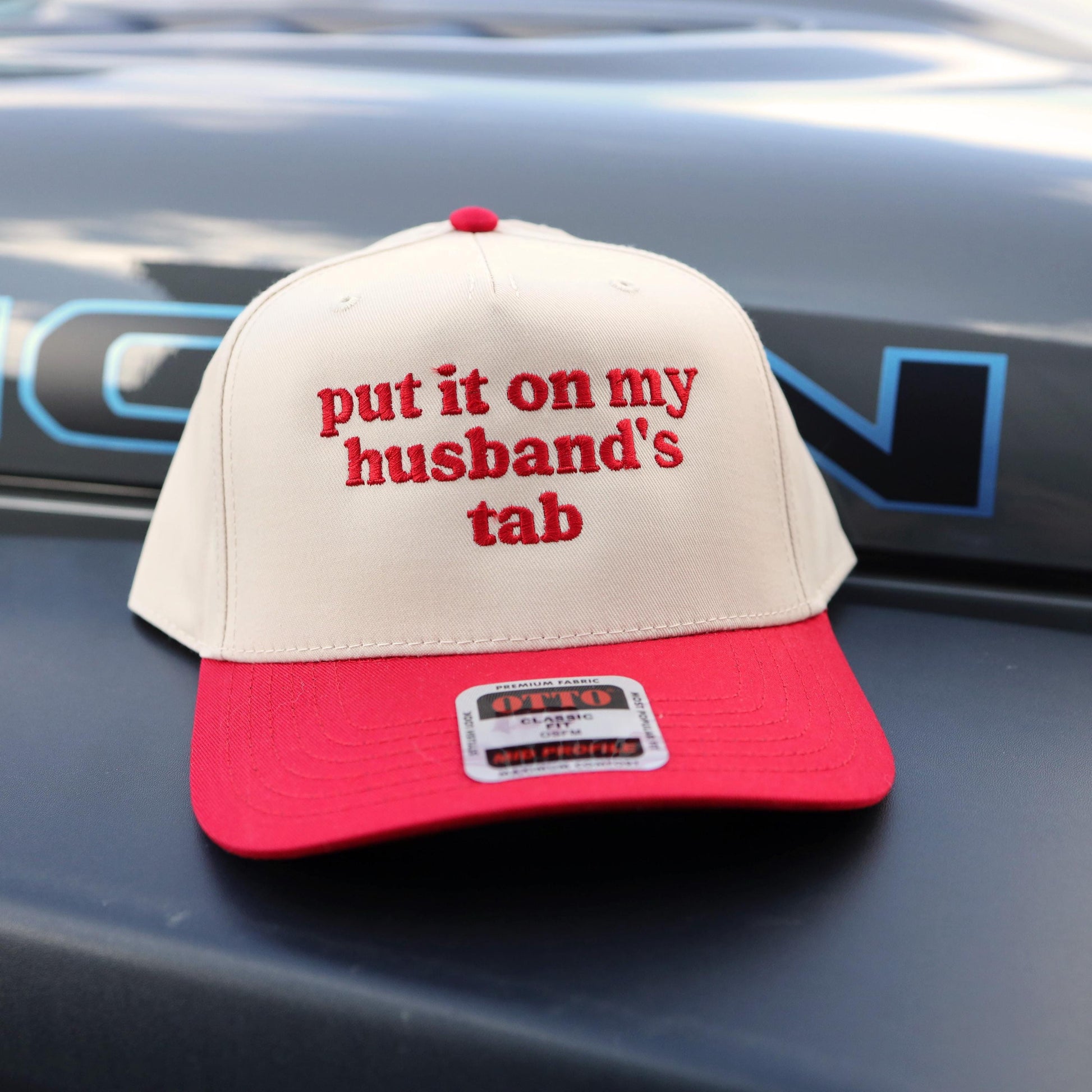 Funny embroidered trucker hat that says put it on my husband's tab with red embroidery and red bill

